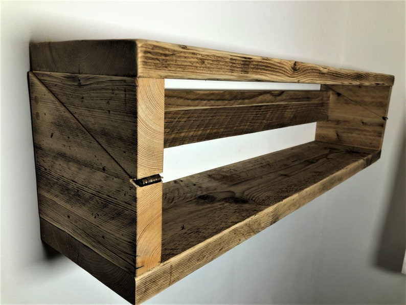 May include: A rustic wooden shelf with two shelves, made from reclaimed wood. The shelf is mounted to the wall and has a triangular design on the left side.