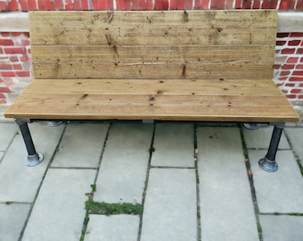 May include: A wooden bench with a rustic finish and a natural wood color. The bench has a back and a seat made of thick planks of wood. The bench is supported by four black metal legs.
