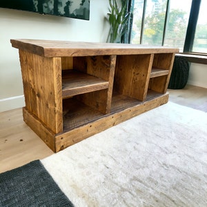May include: A rustic wooden entertainment unit with three open shelves. The shelves are made of reclaimed wood and have a natural finish. The entertainment unit is sitting on a white rug.