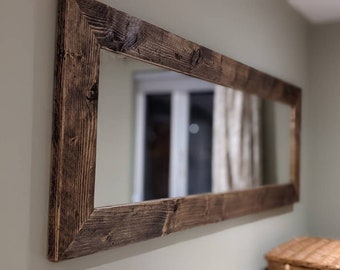 May include: A large rectangular mirror with a dark brown wooden frame. The frame is made of reclaimed wood with a rustic finish.
