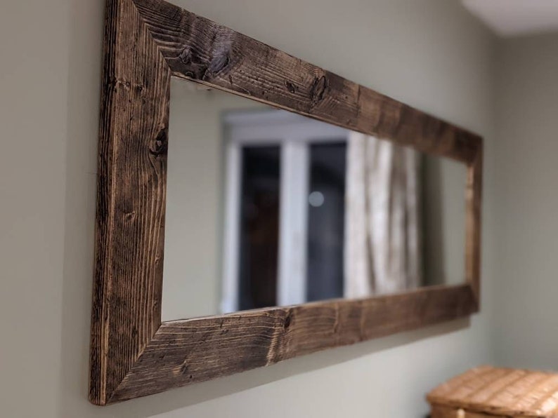 Op de afbeelding: Een grote rechthoekige spiegel met een donkerbruine houten lijst. De lijst is gemaakt van gerecycled hout met een rustieke afwerking.