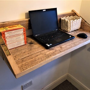 May include: A wooden wall-mounted desk with a laptop, a white woven basket, and a computer mouse. The desk is made of reclaimed wood and has a natural finish. There are several books stacked on the left side of the desk.