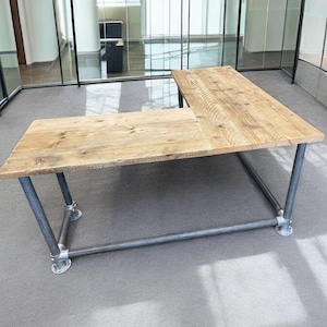 Può includere: Una grande scrivania a forma di L con un piano in legno rustico e una struttura in metallo. La scrivania è realizzata in legno riciclato e ha un aspetto naturale e grezzo. La struttura in metallo è realizzata con tubi di stile industriale ed è verniciata di nero.