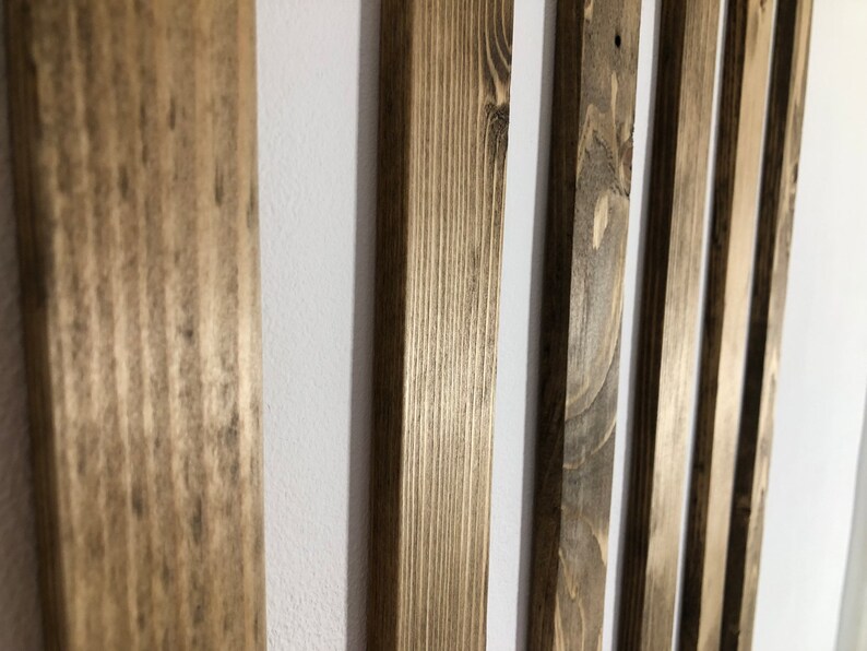 May include: Close-up of vertical wooden slats with a natural, weathered finish. The wood grain is visible, and the slats are arranged against a white background. The varying tones of brown and gray create a rustic aesthetic.