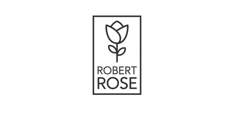 May include: A black and white logo featuring a stylized rose with the text "ROBERT ROSE" in a rectangular frame. The rose is depicted with a simple outline, and the text is in a clean, sans-serif font.