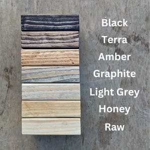 May include: A vertical arrangement of seven wooden blocks, each stained a different color. The colors are black, terra, amber, graphite, light grey, honey, and raw. The names of the colors are listed in white text to the right of the blocks.
