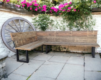 May include: A wooden corner bench with a rustic finish and black metal legs. The bench is set against a white brick wall with a wheel behind it.