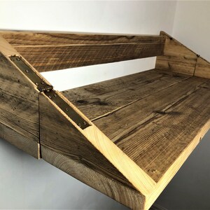 May include: A rustic wooden wall-mounted shelf with a fold-down design. The shelf is made of reclaimed wood and has a natural finish. The shelf is supported by two triangular brackets and has a metal hinge.