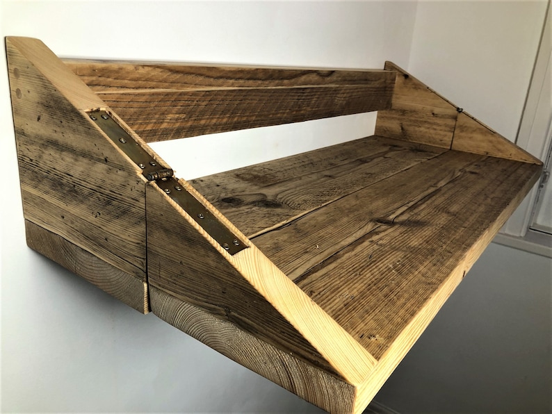 May include: A rustic wooden wall-mounted shelf with a fold-down design. The shelf is made of reclaimed wood and has a natural finish. The shelf is supported by two triangular brackets and has a metal hinge.