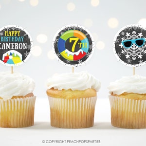 May include: Three cupcakes with black and white cupcake toppers. The toppers feature a snowflake with sunglasses, a colorful inner tube with the number 7 and the words "7th", and the words "Happy Birthday Cameron".