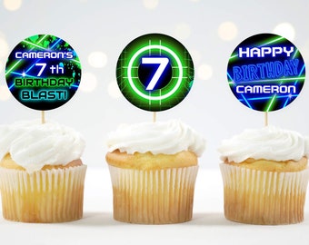 May include: Three cupcakes with green, blue, and black frosting. Each cupcake has a round, printed paper topper with a neon green and blue design. The toppers say "Cameron's 7th Birthday Blast!" and "Happy Birthday Cameron".