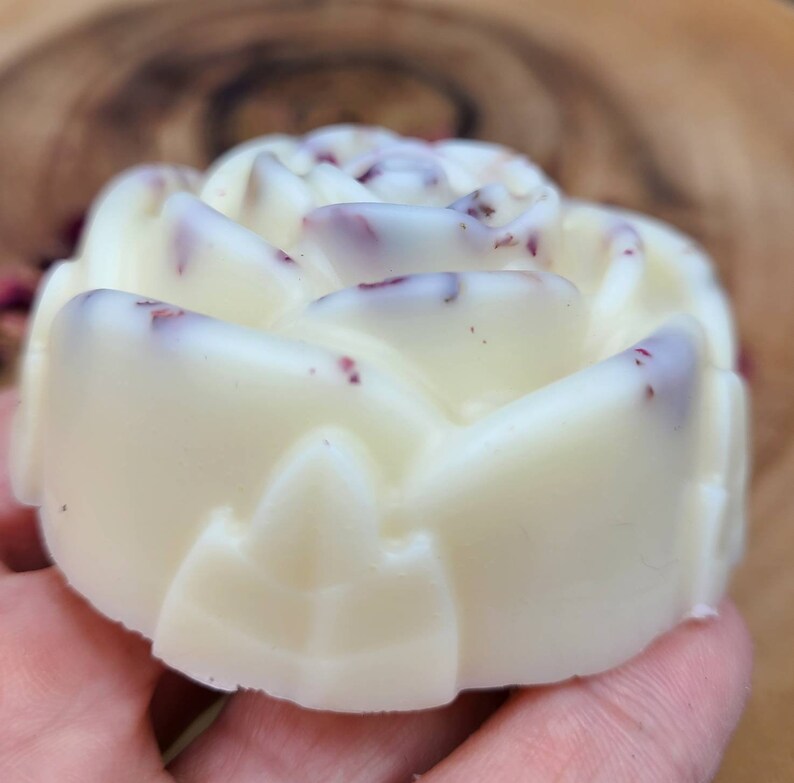 May include: A white rose-shaped soap with pink and red flecks throughout. The soap is in the shape of a rose with a detailed design.