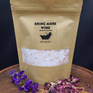 May include: A brown paper bag with a white label that reads "Bring More Wine - Or Leave Me Alone" and a cartoon bathtub with a person in it. The label also says "fizzy bath salts". The bag is filled with white bath salts.