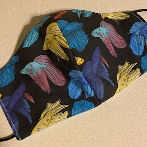 May include: A black fabric face mask with a repeating pattern of colorful betta fish. The fish are in shades of blue, yellow, and pink.