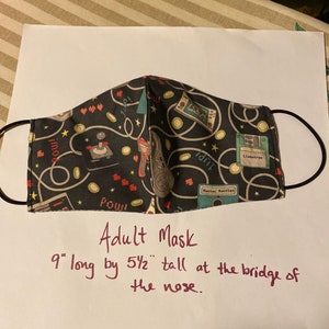 May include: Adult face mask with a black background and a pattern of retro video game controllers, stars, and text. The mask is 9 inches long and 5.5 inches tall at the bridge of the nose.