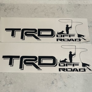 May include: Two black vinyl decals with the text "TRD OFF ROAD" and a silhouette of a person fishing with a dog.