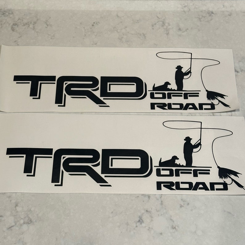 May include: Two black vinyl decals with the text "TRD OFF ROAD" and a silhouette of a person fishing with a dog.