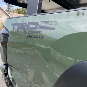 May include: A green pickup truck with a black "TRD OFF ROAD" decal and an American flag graphic on the side.
