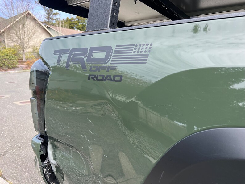 May include: A green pickup truck with a black "TRD OFF ROAD" decal and an American flag graphic on the side.