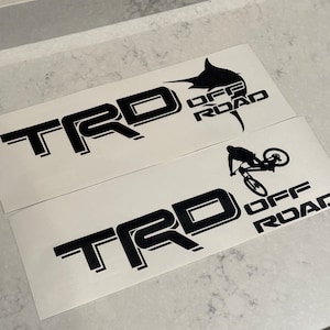 May include: Two black and white vinyl decals with the text "TRD OFF ROAD" and a graphic of a marlin fish and a mountain biker.