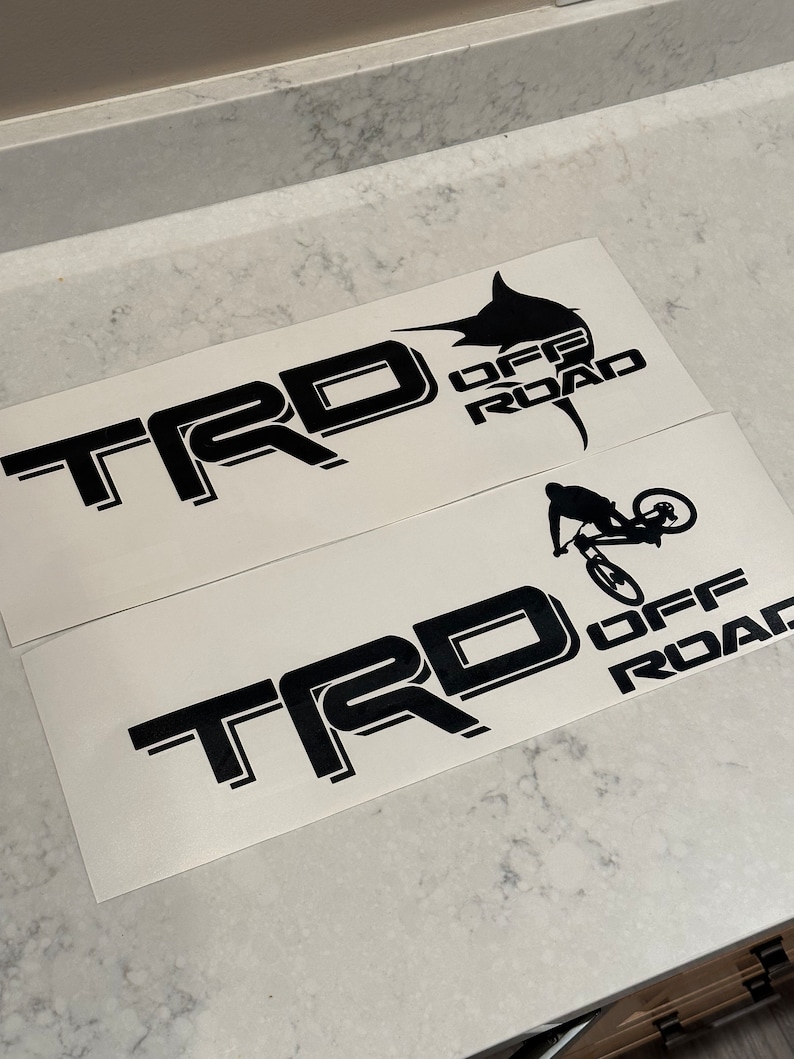 May include: Two black and white vinyl decals with the text "TRD OFF ROAD" and a graphic of a marlin fish and a mountain biker.