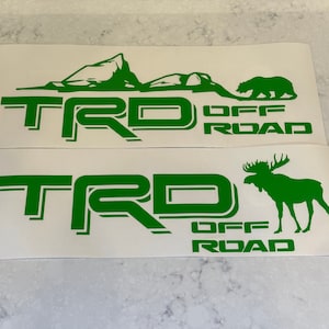 May include: Two green vinyl decals with the text "TRD OFF ROAD" and a mountain scene with a bear on the top decal and a moose on the bottom decal.
