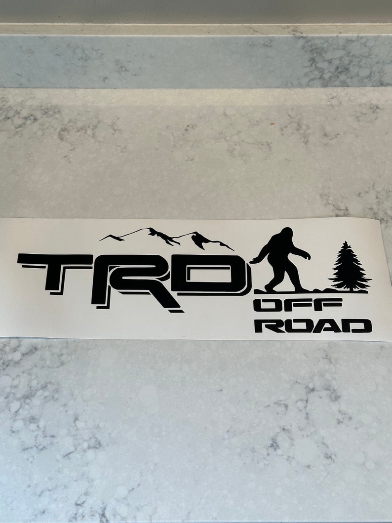 May include: Black and white decal with the text "TRD OFF ROAD" and a silhouette of a mountain range, a Bigfoot, and a pine tree.