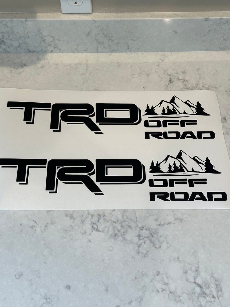 May include: Two black vinyl decals with the text "TRD OFF ROAD" and a mountain range graphic.