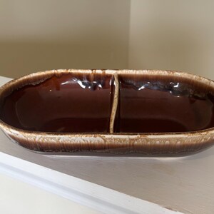 May include: A brown ceramic divided serving dish with a glossy finish. The oval dish is split into two sections by a vertical divider. The rim has a lighter, textured edge. The dish is likely vintage and suitable for serving snacks or appetizers.