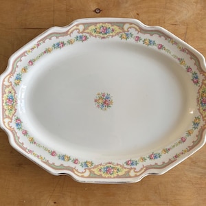 May include: An oval ceramic serving platter with a scalloped edge, featuring a cream-colored center with a small floral bouquet and a decorative border of pink, yellow, and blue flowers on a pale yellow and green vine pattern.