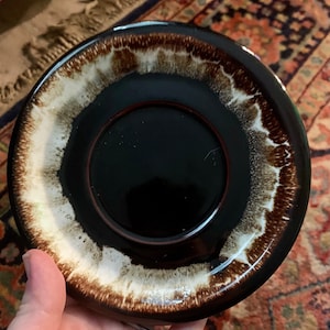May include: A brown and white ceramic saucer with a black center. The saucer has a mottled glaze with brown and white streaks.