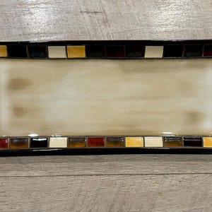 May include: A rectangular serving tray with a black rim and a mosaic design of brown, red, yellow, and white squares.