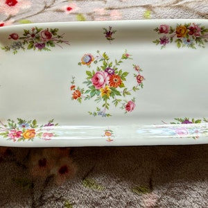 May include: Rectangular serving dish with a cream-colored background. The dish is decorated with floral patterns in shades of pink, yellow, purple, and orange. The flowers are arranged in clusters and along the edges of the dish.