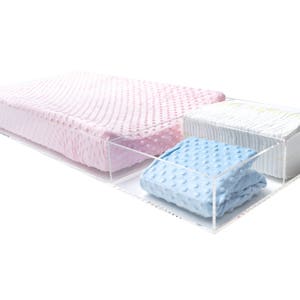 Puede incluir: Cajas de almacenamiento de acrílico transparente con una manta estampada en rosa y azul y una pila de pañales blancos.
