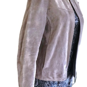 May include: A light purple suede jacket with a zipper closure. The jacket has a slightly fitted silhouette and a stand-up collar.
