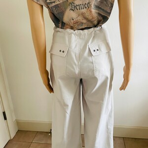 May include: Light gray wide-leg cropped pants with two large pockets on the back. Each pocket has two silver buttons.