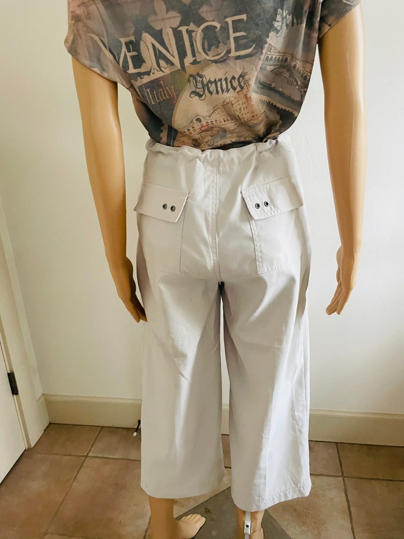 May include: Light gray wide-leg cropped pants with two large pockets on the back. Each pocket has two silver buttons.