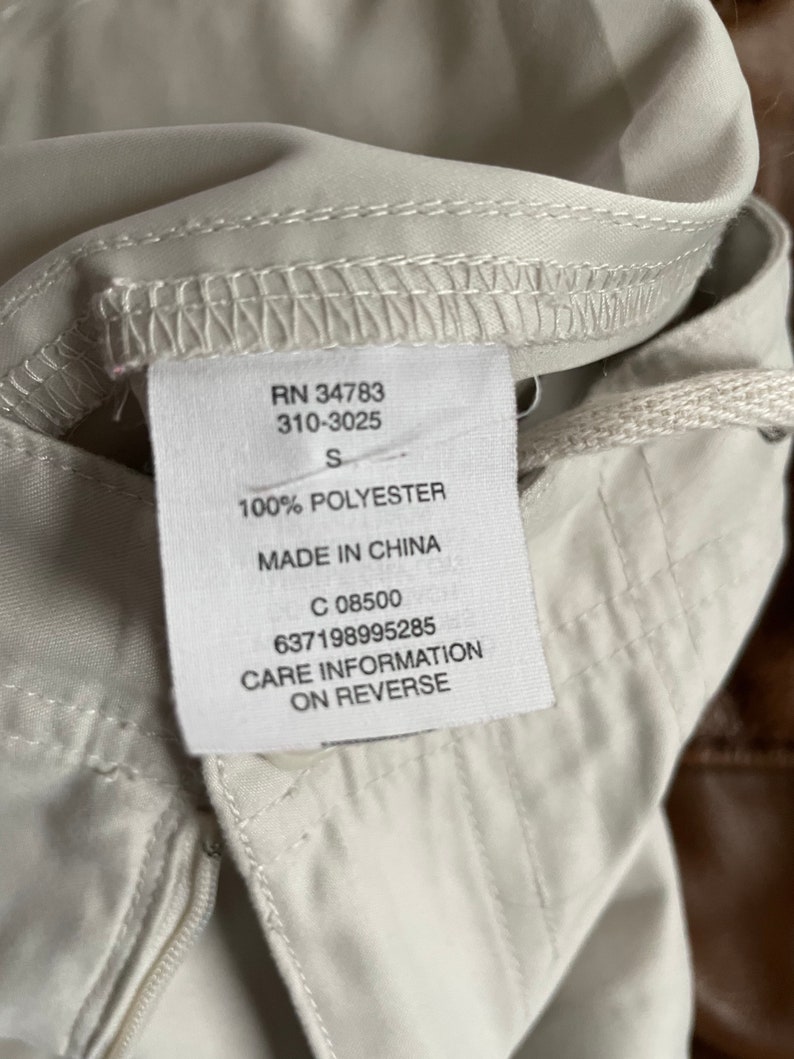 May include: White clothing tag with black text. The tag says "RN 34783 310-3025 S 100% POLYESTER MADE IN CHINA C 08500 637198995285 CARE INFORMATION ON REVERSE".