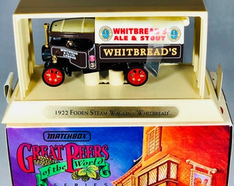May include: A Matchbox Great Beers of the World Series die-cast model of a 1922 Foden Steam Wagon, painted brown and black, with a white and red Whitbread's Ale & Stout advertisement on the side. The model is displayed in a clear plastic case with a white base.