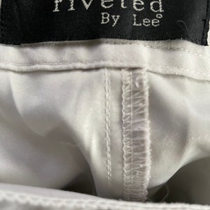 May include: White pants with a black label that reads "riveted By Lee"