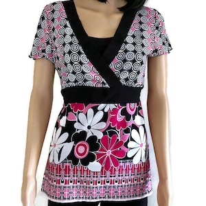 May include: A black and white patterned short-sleeved top with a pink and white floral print on the bottom. The top has a V-neck and a black belt.