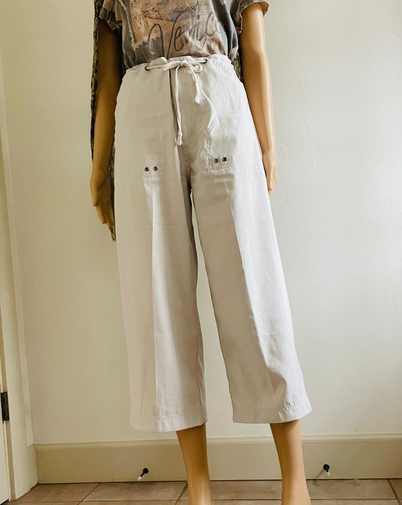 May include: White cropped pants with a drawstring waist and two pockets. The pants have a relaxed fit and are made of a lightweight fabric.