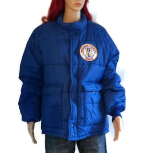 Op de afbeelding: Een blauwe pufferjas met een gele en rode patch waarop "Eastside Lightning" en "Front 17" staat.