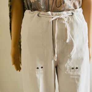 May include: White drawstring pants with a relaxed fit and two silver eyelets on each side of the leg.