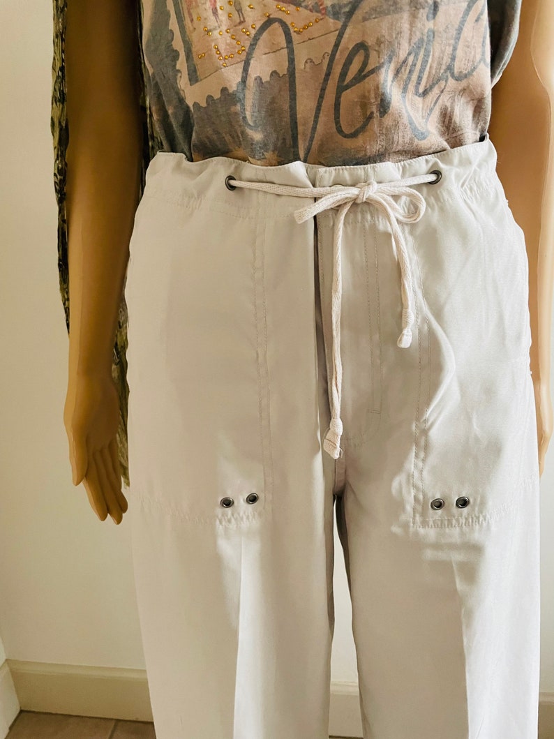 May include: White drawstring pants with a relaxed fit and two silver eyelets on each side of the leg.