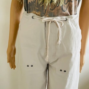 May include: White drawstring pants with two sets of black button accents on the front. The pants have a relaxed fit and a casual style.