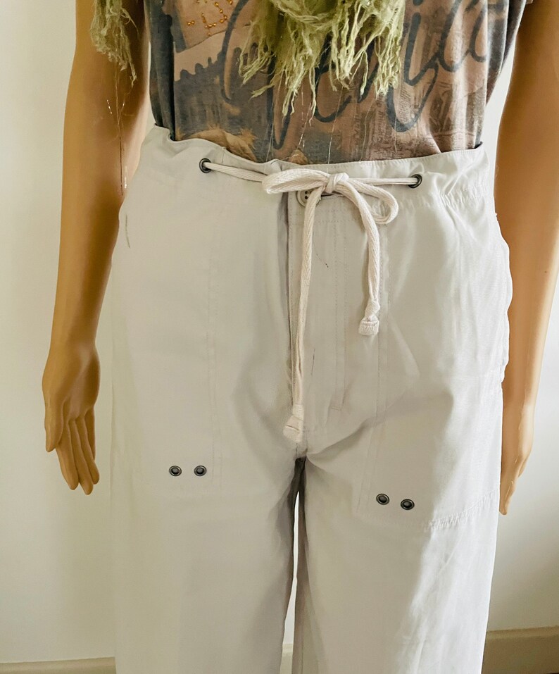 May include: White drawstring pants with two sets of black button accents on the front. The pants have a relaxed fit and a casual style.
