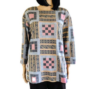 May include: A gray, long-sleeved shirt with a geometric pattern in shades of pink, gold, and black. The pattern features squares, checkered designs, and paisley-like motifs.