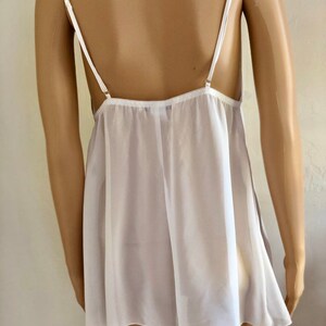 K&ouml;nnte beinhalten: Wei&szlig;es, durchsichtiges Schlupfkleid mit d&uuml;nnen Tr&auml;gern. Das Kleid hat einen lockeren, flie&szlig;enden Schnitt und einen gewellten Saum.