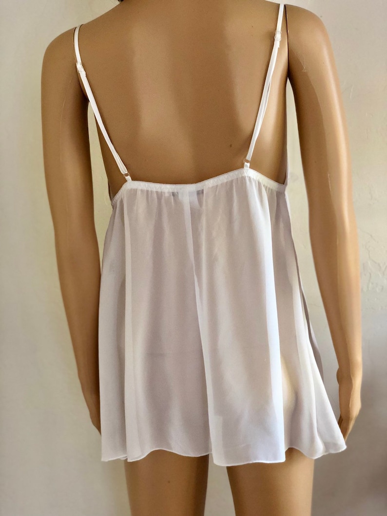 K&ouml;nnte beinhalten: Wei&szlig;es, durchsichtiges Schlupfkleid mit d&uuml;nnen Tr&auml;gern. Das Kleid hat einen lockeren, flie&szlig;enden Schnitt und einen gewellten Saum.